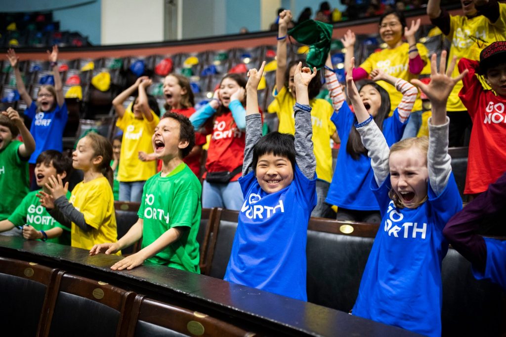 Excited young boys and girls cheering in three rows of seats