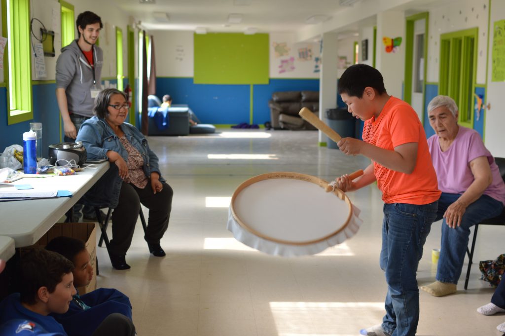 Camp participant playing the drum surrounded by community elders