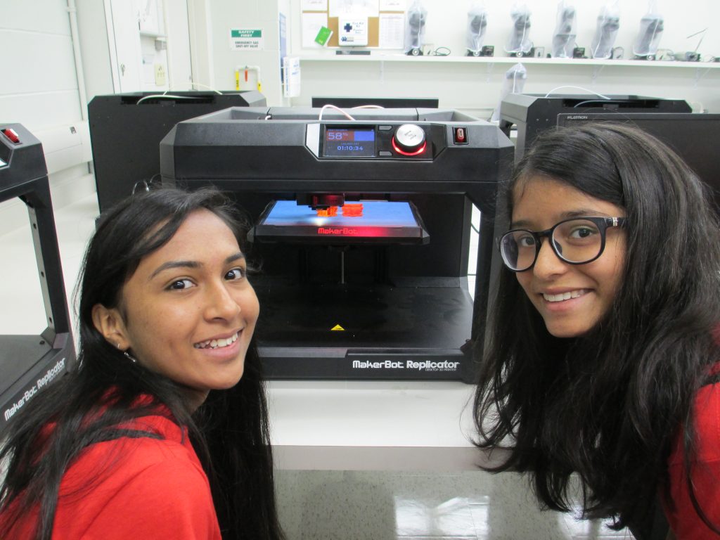 Two girls standing of a 3D printer