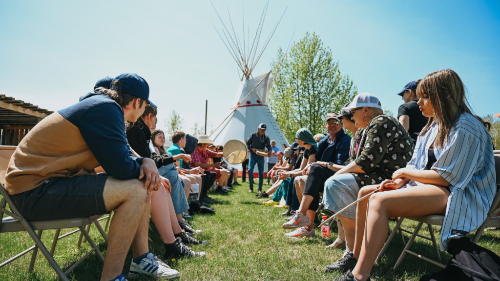 Students sitting outside in a circle during a drumming ceremony