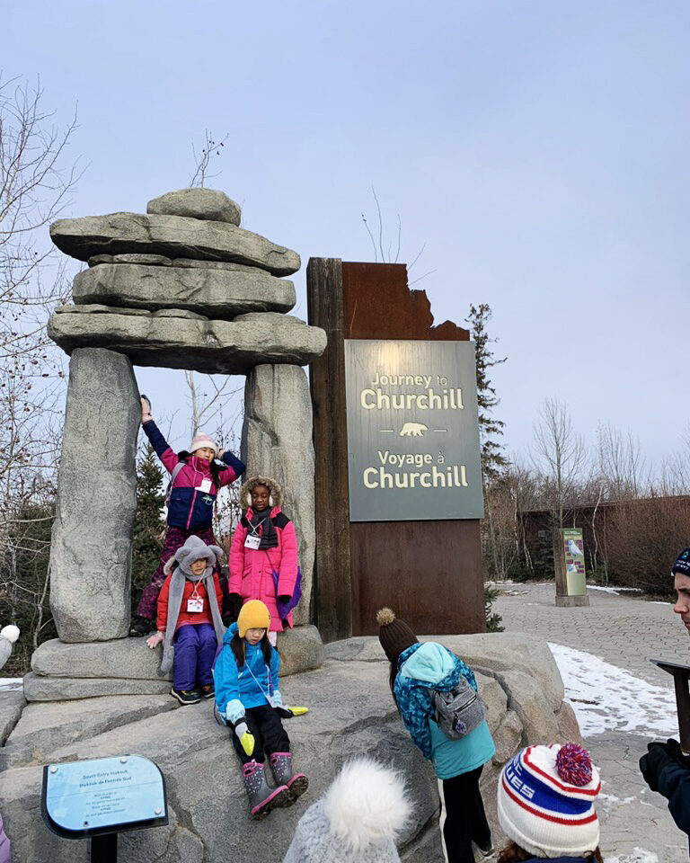 A group of young girls in front of a Churchill Voyage sign at the Assiniboine Park Zoo