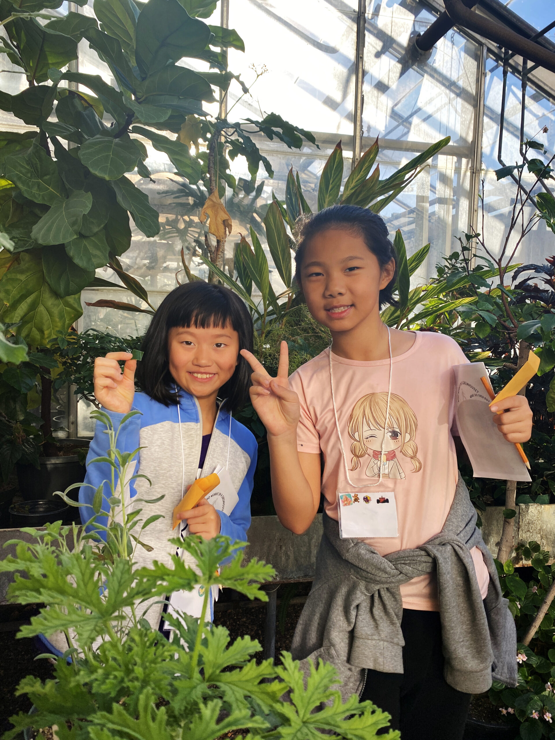Two girls at a greenhouse looking at a green plant